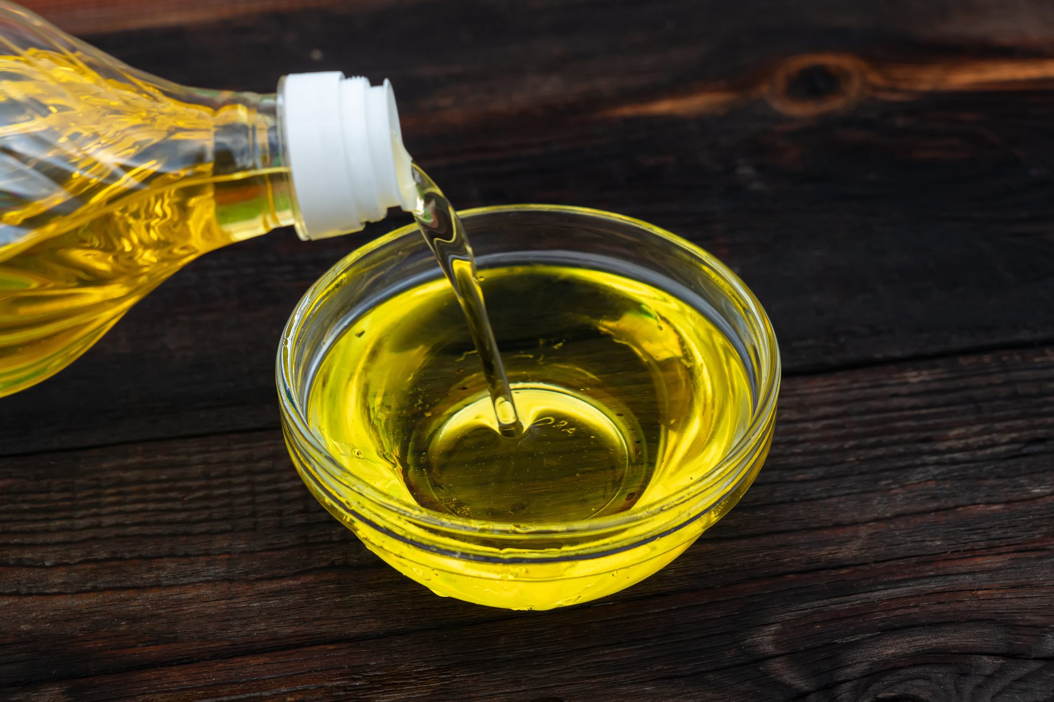 Olio viene versato da una bottiglia a una ciotola di vetro